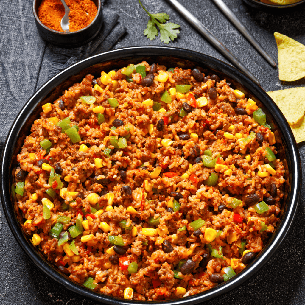 Southwest ground beef skillet in a black bowl with black beans, corn, green bell peppers, and rice, served with a side of tortilla chips and spices. A vibrant, flavorful one-pan meal ideal for family dinners
